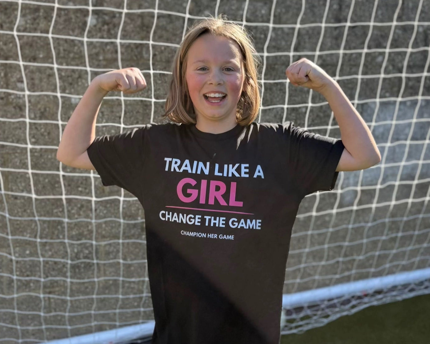 Girl wearing a 'Train Like a Girl' shirt in front of a soccer goal