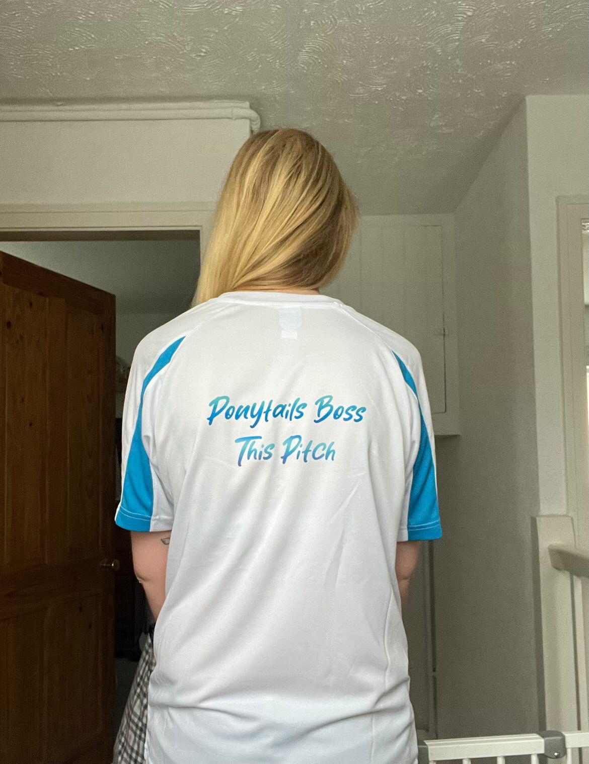 Person wearing a white and blue shirt with text in a room.