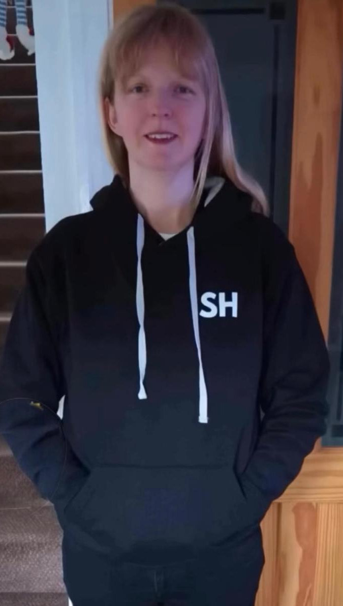 Person wearing a black hoodie with 'SH' logo indoors