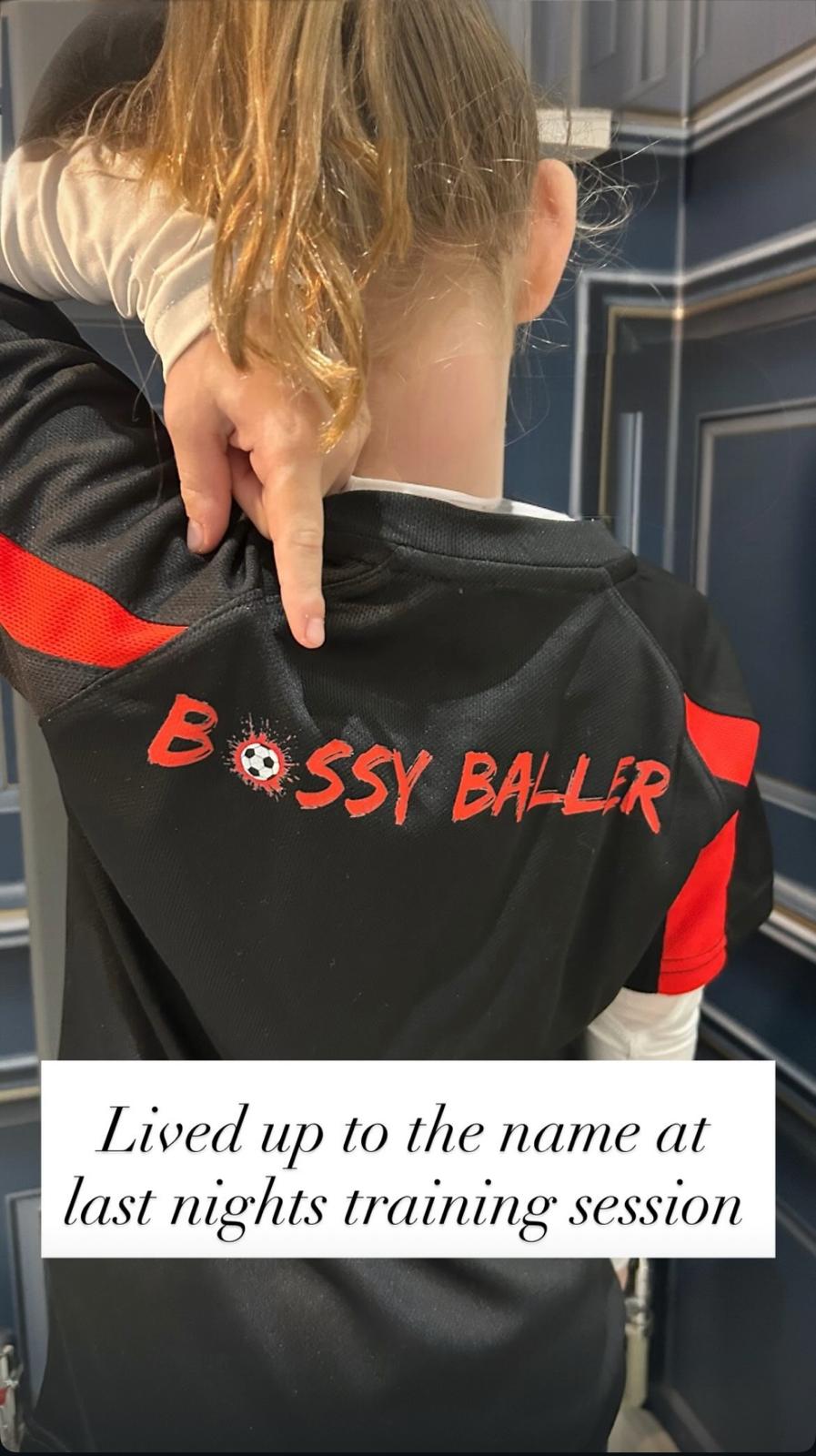 Person wearing a black jacket with 'Bossy Baller' text, standing in a room.