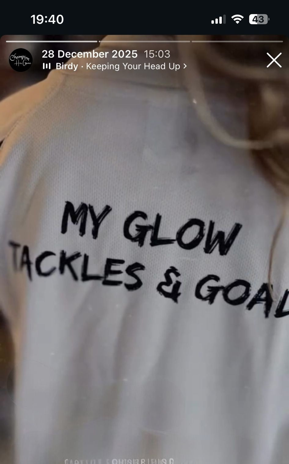 White sweatshirt with text 'MY GLOW TACKLES & GOALS' on a blurred background