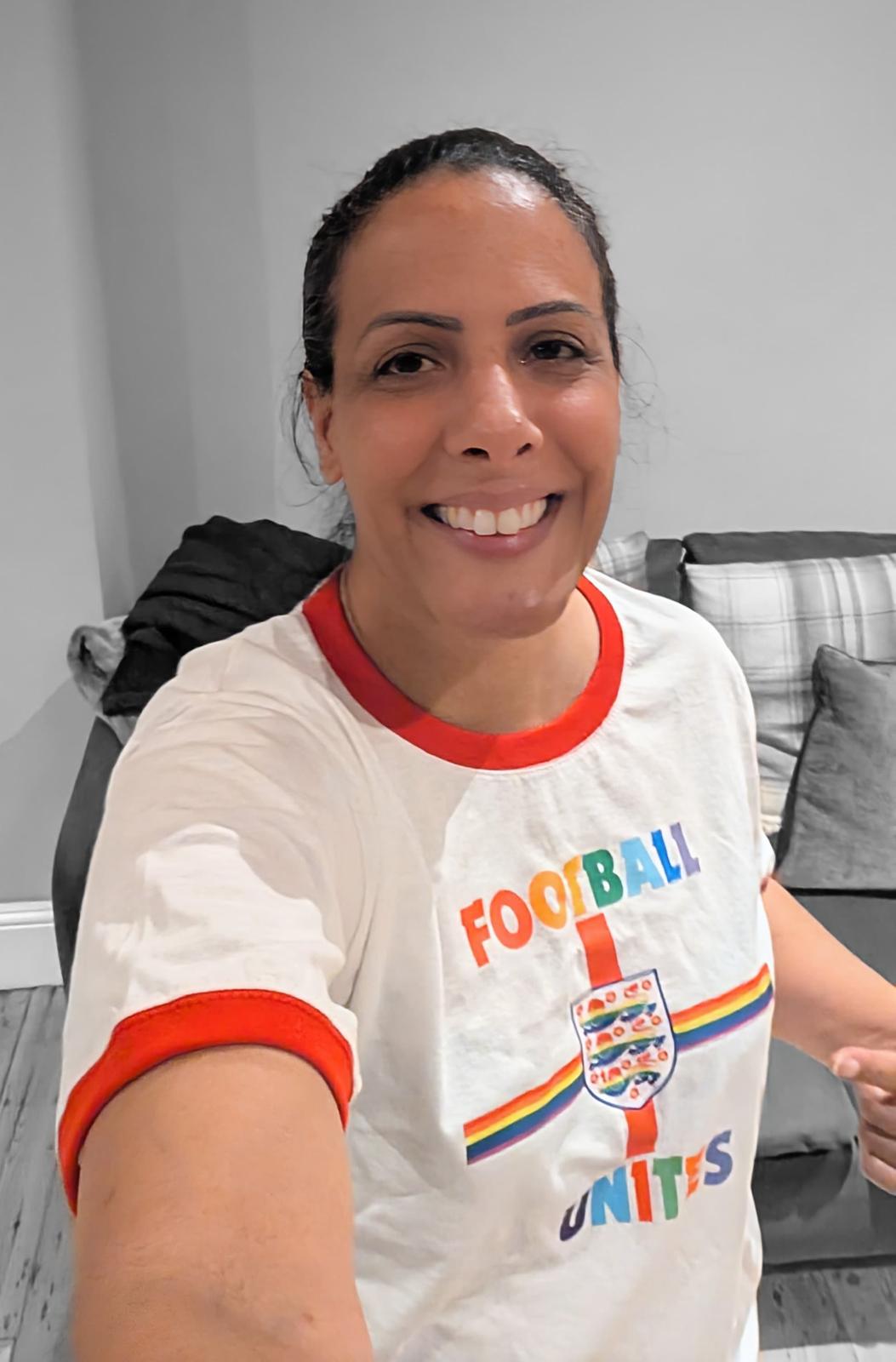 Woman wearing a white t-shirt with colorful text and graphics, sitting in a room.