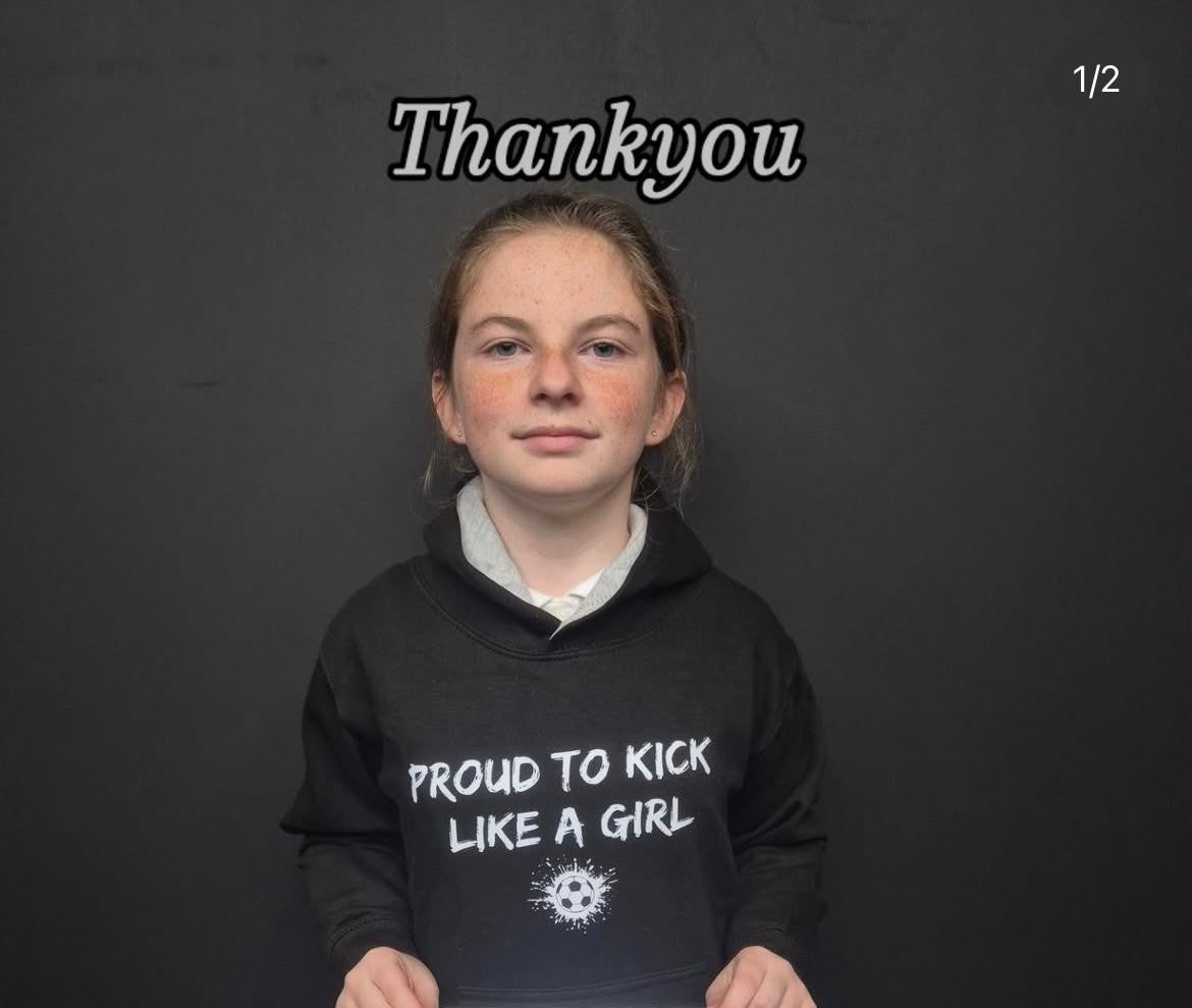 Person wearing a black hoodie with 'Proud to kick like a girl' text on a dark background
